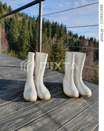 Two pairs of white rubber boots stand on a wooden terrace 135681998