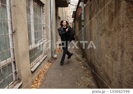 Young person joyfully walking through a narrow alley surrounded by weathered buildings and fallen leaves in autumn Young person joyfully walking through a narrow alley surrounded by weathered buildings and fallen leaves in autumn 135682599