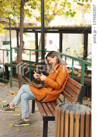 Enjoying a sunny afternoon working on a laptop in a park surrounded by autumn leaves Enjoying a sunny afternoon working on a laptop in a park surrounded by autumn leaves 135682807