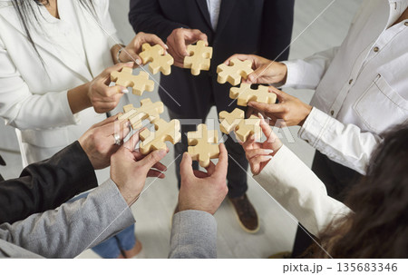 Team building and support, hands of business people group holding wooden puzzle pieces in circle Team building and support, hands of business people group holding wooden puzzle pieces in circle 135683346