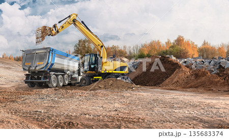 Construction workers use a loader and excavator to move dirt and materials at a site with trees and rocks in the background during daytime 135683374