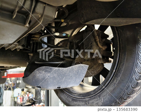 A mechanic inspects the suspension system and wheel of a vehicle in an auto repair shop. Tools and equipment are visible in the background 135683390