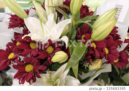 A variety of red and white flowers are arranged together in a display. The bouquet includes lilies and chrysanthemums in a retail setting 135683395