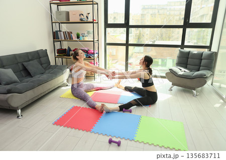 Two friends practicing yoga together in a bright, modern living room filled with colorful mats Two friends practicing yoga together in a bright, modern living room filled with colorful mats 135683711