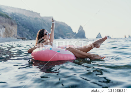 Woman Ocean Float Happy woman relaxing on a pink donut float in the calm sea near scenic cliffs. 135686834