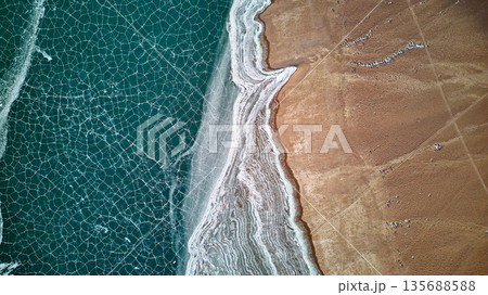 Aerial view of cracked ice on lake with frozen shore and brown land Aerial view of cracked ice on lake with frozen shore and brown land 135688588