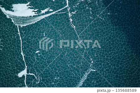 Abstract aerial top down view of cracked ice on dark blue lake water. Abstract aerial top down view of cracked ice on dark blue lake water. 135688589