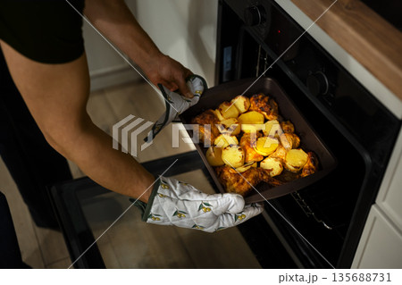 Man cooking dinner at his home kitchen, taking ready meal out of oven 135688731