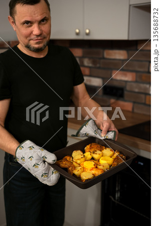 Senior man cooking dinner at his home kitchen, taking ready meal out of oven 135688732
