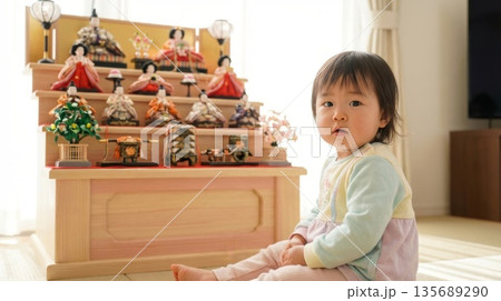 リビングに飾られた木製のナチュラルなひな人形の前にちょこんと座る可愛い女の子 リビングに飾られた木製のナチュラルなひな人形の前にちょこんと座る可愛い女の子 135689290