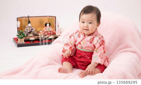 ピンク色のふわふわな椅子に座って笑顔を見せる袴姿の赤ちゃんとひな人形 135689295