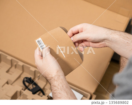 Persons hands carefully opening a brown cardboard sleeve with a barcode, removed from new product packaging, illustrating consumer unboxing and delivery experience Persons hands carefully opening a brown cardboard sleeve with a barcode, removed from new product packaging, illustrating consumer unboxing and delivery experience 135689802