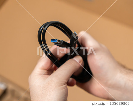Human hands holding a black USB cable, showcasing both modern Type-A and Type-C connectors for universal device connectivity and efficient data transfer 135689803