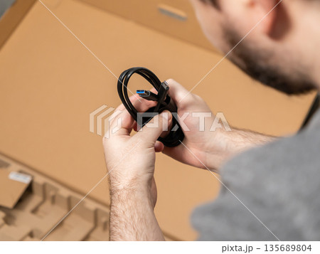 Person holding a black USB 3.0 cable while unboxing a new technology product, symbolizing connection, setup, and modern digital device installation 135689804