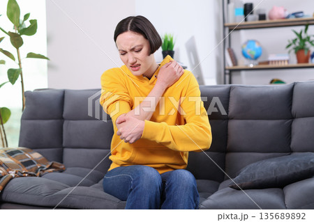 Feeling discomfort while seated on a cozy sofa in a bright living room during a casual afternoon Feeling discomfort while seated on a cozy sofa in a bright living room during a casual afternoon 135689892