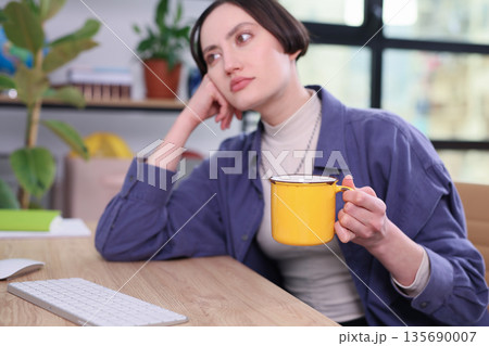 Thoughtful moment in a cozy workspace with a cup of tea in hand during a quiet afternoon Thoughtful moment in a cozy workspace with a cup of tea in hand during a quiet afternoon 135690007