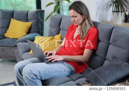 Woman working on laptop seated comfortably in cozy living room during midday Woman working on laptop seated comfortably in cozy living room during midday 135690561