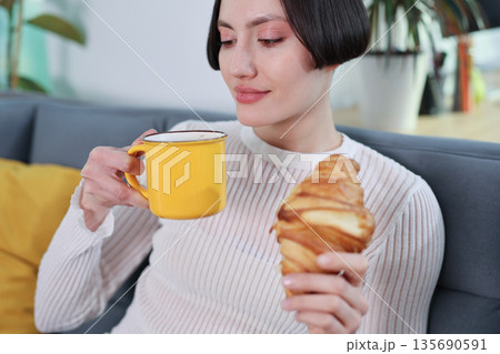 Enjoying a cozy morning with coffee and a fresh croissant in a stylish living room Enjoying a cozy morning with coffee and a fresh croissant in a stylish living room 135690591