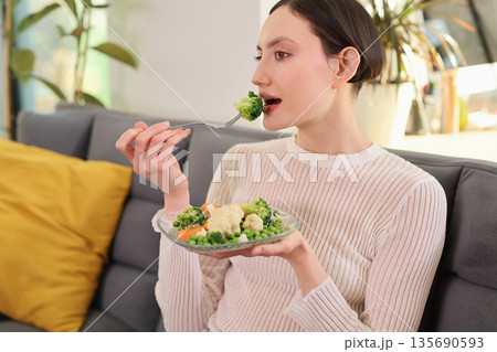 Eating a healthy plate of fresh vegetables while relaxing on a cozy sofa during a sunny afternoon indoors Eating a healthy plate of fresh vegetables while relaxing on a cozy sofa during a sunny afternoon indoors 135690593