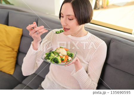 Enjoying a healthy meal of colorful vegetables while relaxing at home in a cozy living room Enjoying a healthy meal of colorful vegetables while relaxing at home in a cozy living room 135690595