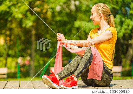 Girl doing exercise outdoor, using resistance fit band. 135690959