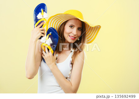 Woman in big yellow summer hat holds flip flops 135692499