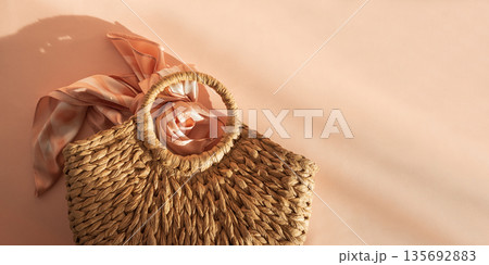 Woven Straw Handbag with Silky Scarf. Elegant Summer Fashion Flatlay on Peach Background Woven Straw Handbag with Silky Scarf. Elegant Summer Fashion Flatlay on Peach Background 135692883
