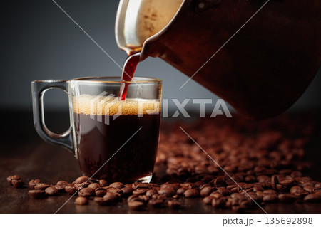 Black coffee is poured into a glass cup. Black coffee is poured into a glass cup. 135692898