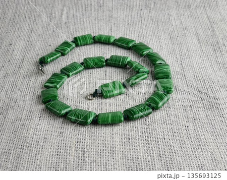 Handmade beads made of green malachite on burlap background Handmade beads made of green malachite on burlap background 135693125