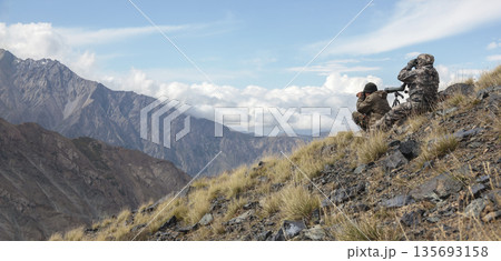 Hunters with binoculars and an optical tube to search for hunting objects on the mountainside. Hunters with binoculars and an optical tube to search for hunting objects on the mountainside. 135693158