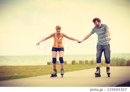Young couple on roller skates riding outdoors Young couple on roller skates riding outdoors 135693307
