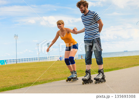 Young couple on roller skates riding outdoors Young couple on roller skates riding outdoors 135693308