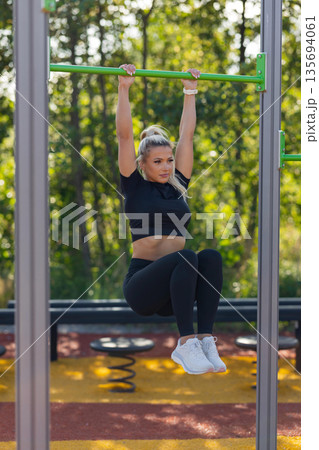 Woman practicing outdoor strength training on fitness equipment in park setting 135694061