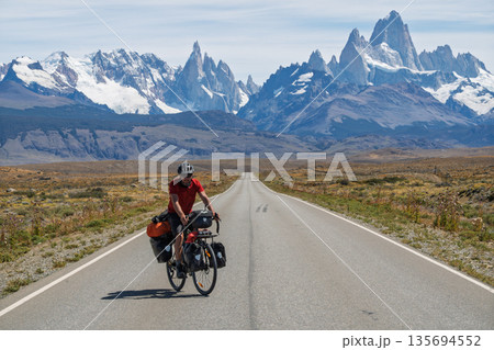 Cyclist riding straight road toward massive Mount Fitz Roy, Patagonia, Argentina Cyclist riding straight road toward massive Mount Fitz Roy, Patagonia, Argentina 135694552