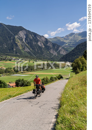 Cyclist cycle touring through green mountain valley in Swiss Alps, Switzerland Cyclist cycle touring through green mountain valley in Swiss Alps, Switzerland 135694559