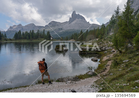 Hiker admiring Becco di Mezzodi reflection at Lago Federa, Dolomites Hiker admiring Becco di Mezzodi reflection at Lago Federa, Dolomites 135694569