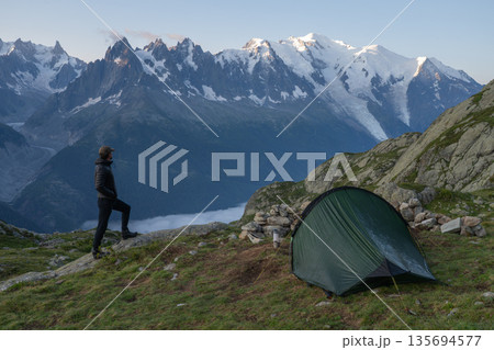 Hiker standing by tent viewing Mont Blanc massif and Bossons Glacier, France Hiker standing by tent viewing Mont Blanc massif and Bossons Glacier, France 135694577