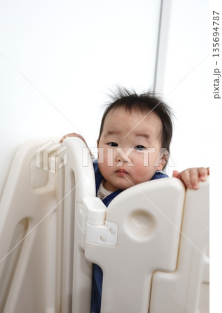 ベビーゲート越しに覗く0歳の女の子の赤ちゃん。 ベビーゲート越しに覗く0歳の女の子の赤ちゃん。 135694787