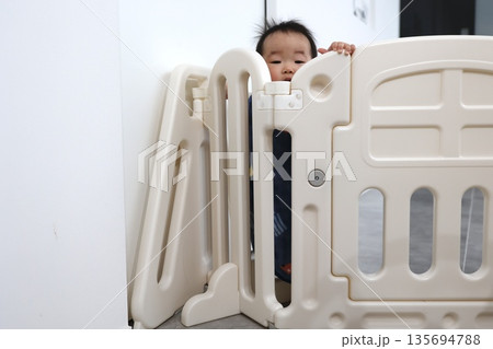 ベビーゲート越しに覗く0歳の女の子の赤ちゃん。 ベビーゲート越しに覗く0歳の女の子の赤ちゃん。 135694788