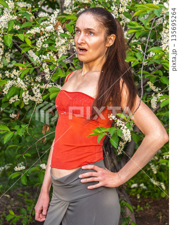 Young woman sneezes in the park against the background of a flowering tree. Allergy to pollen concept. 135695264