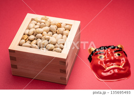 赤背景に節分の豆とお面を配置した静物写真 135695493