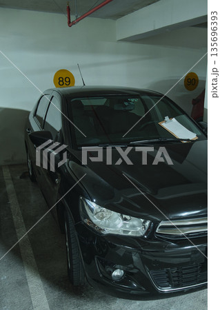 Black sedan parked in underground parking garage spot 135696393