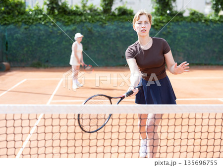 Middle aged and senior women plays tennis on open court with opponent. Middle aged and senior women plays tennis on open court with opponent. 135696755