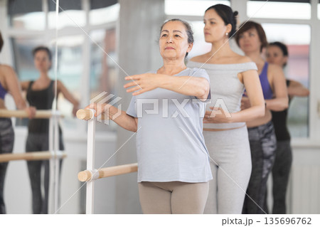 Senior woman practicing first position at barre in ballet studio 135696762