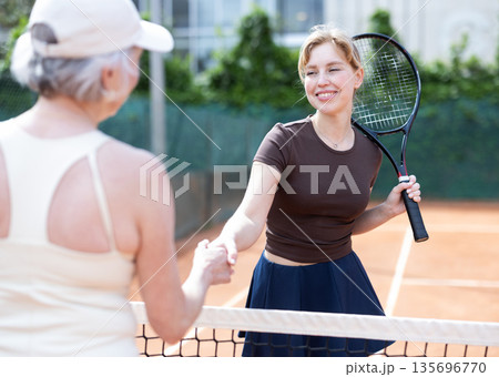 Young and senior women tennis players shake hands across net. 135696770