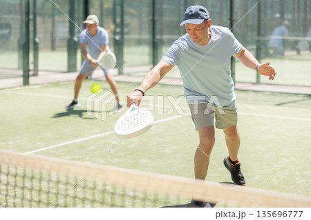 Elderly and adult men playing doubles padel Elderly and adult men playing doubles padel 135696777