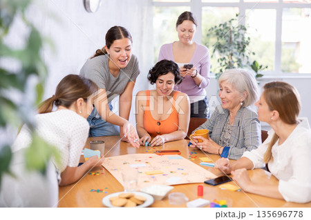 Group of cheerful female colleagues playing board game in office Group of cheerful female colleagues playing board game in office 135696778