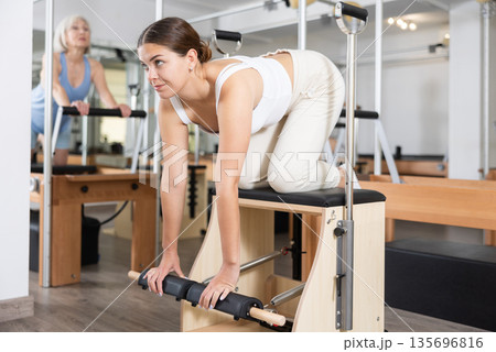 Young woman making pilates exercising while standing on knees using Wanda chair machine 135696816