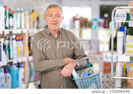 Elderly man selects various household cleaning products for cleaning the house with full basket of various purchases Elderly man selects various household cleaning products for cleaning the house with full basket of various purchases 135696840