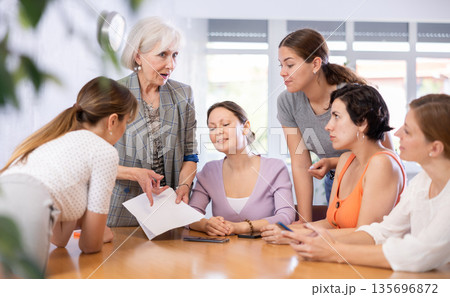 Women discuss documents sitting at table in office 135696872